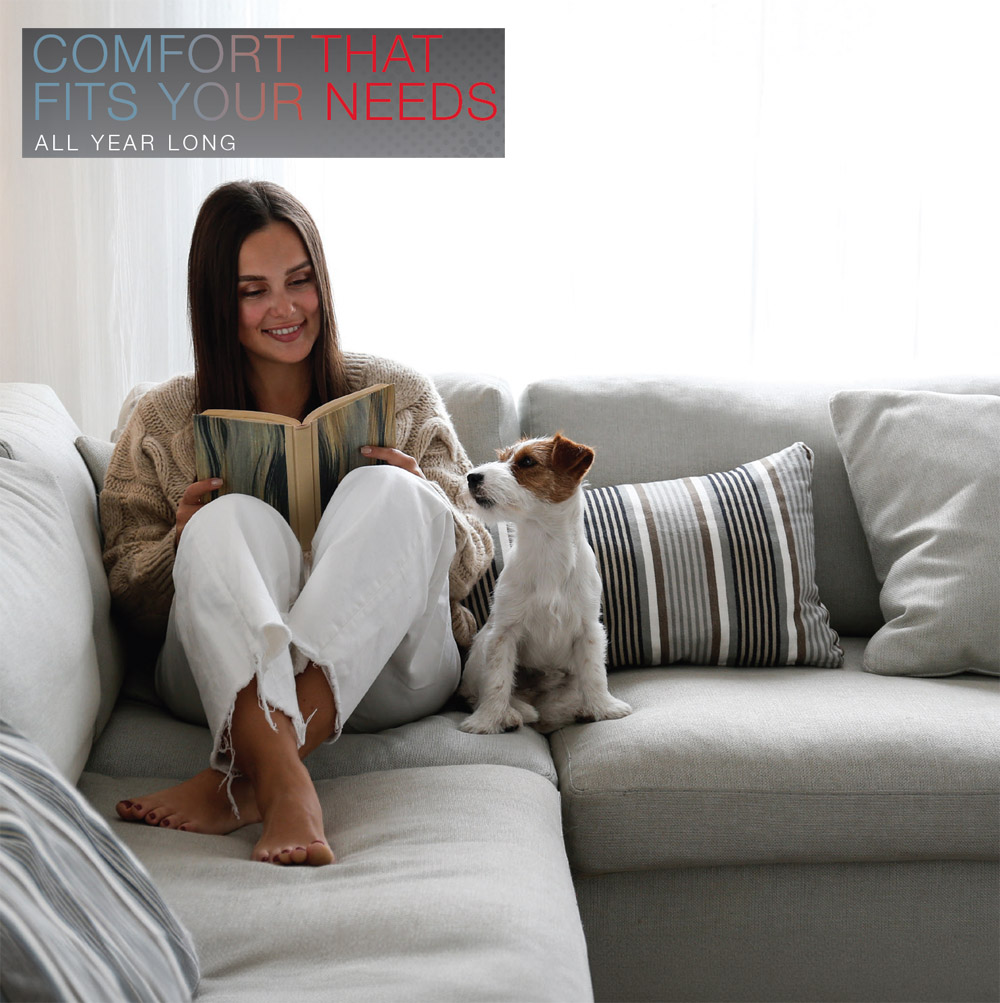 COMFORT THAT FITS YOUR NEEDS. ALL YEAR LONG. Woman and pet dog on couch enjoying comfort of Rheem RD18AY Endeavor™ Line Prestige Series Side-Discharge Universal Heat Pump